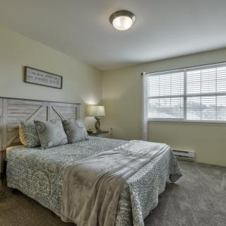A cozy bedroom with a neatly made bed, soft lighting, and natural light streaming through the window.