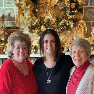 Three women posing happily in front of festive holiday decorations.