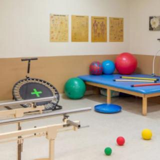 A physical therapy room equipped with various rehabilitation tools, including fitness balls, a trampoline, and parallel bars.
