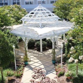 A white gazebo in a lush garden setting with surrounding trees and pathways.