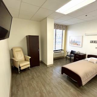 A well-lit and minimalist patient room in a medical facility, featuring a bed, chair, and television.