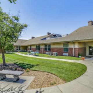 A peaceful outdoor area with a pathway, benches, and green lawn in front of a building.