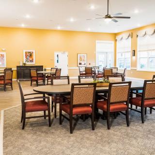 A spacious dining area with multiple tables and chairs, featuring bright orange walls and ample natural light.