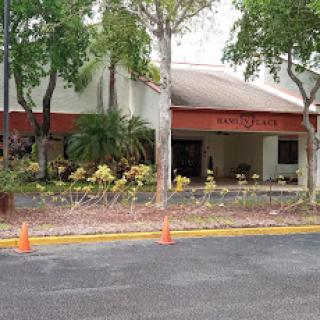 A view of a building entrance surrounded by trees and flowers, with parking cones visible in the foreground.