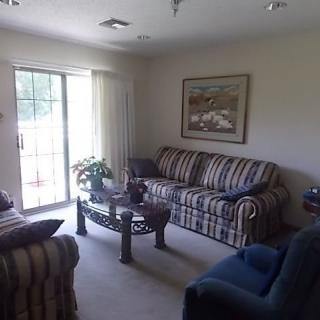 A cozy living room with a striped sofa and armchairs, centered around a glass coffee table, and adorned with wall art.