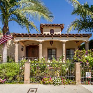 A beautiful house with a lush garden and palm trees on a sunny day.