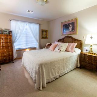 A cozy bedroom with a neatly made bed, wooden furniture, and a window covered by curtains.