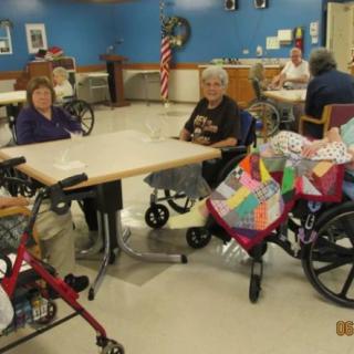 Elderly individuals sitting in a community room, some in wheelchairs, engaging in activities.