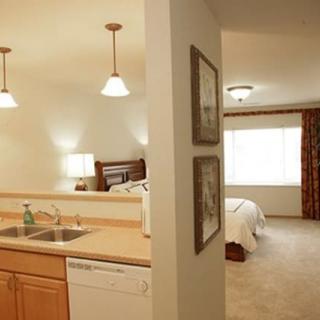 A cozy hotel room featuring a kitchen area with a sink and dishwasher, and a comfortable bedroom.