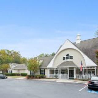A commercial building with a parking lot and cars, surrounded by trees.