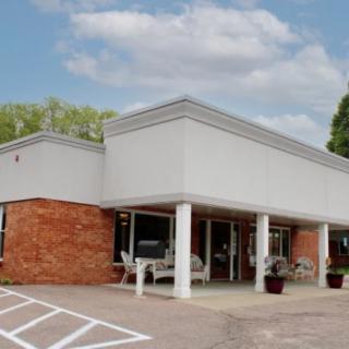 A commercial building with a brick and white exterior, featuring large windows and a parking lot in front.