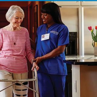 A nurse assists an elderly woman using a walker in a home setting.