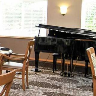 A restaurant interior featuring a grand piano beside dining tables and chairs.