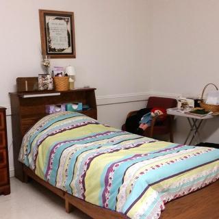A cozy room with a single bed, colorful striped bedding, and basic furnishings.