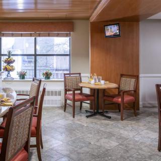 A cozy dining area with tables and chairs, featuring a large window and a wall-mounted television.