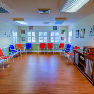 A spacious waiting room with colorful chairs against the walls, featuring a hardwood floor and ample natural light.