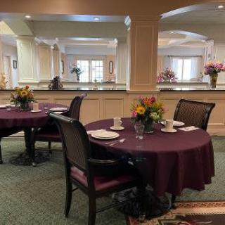 A neatly set dining area with round tables, decorated with floral centerpieces.