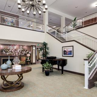 A spacious lobby with a piano and elegant decor, featuring a grand staircase and chandelier.
