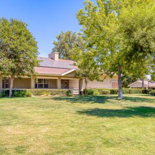 A single-story house with a large front lawn and surrounding trees on a sunny day.