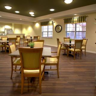 A well-lit dining area with wooden chairs and tables, featuring large windows.