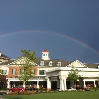 A beautiful rainbow arches over a classic style building against a cloudy backdrop.