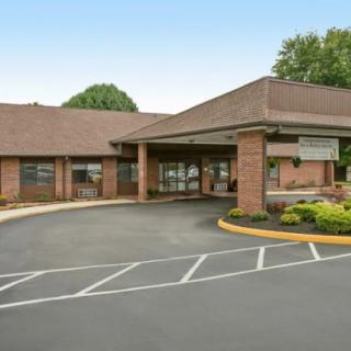 A brick building with an entrance and a circular driveway surrounded by landscaping.