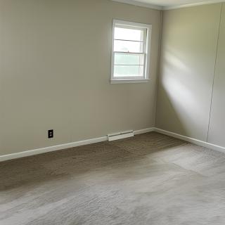 An empty room with beige walls, carpeted floor, and a single window.