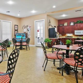 A cozy dining area with tables and chairs, featuring a small kitchen and decorative plants.