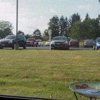 A view of a parking lot filled with cars, surrounded by grass and trees on a sunny day.