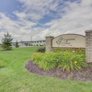 Entrance sign with landscaping and a building in the background under a cloudy sky.
