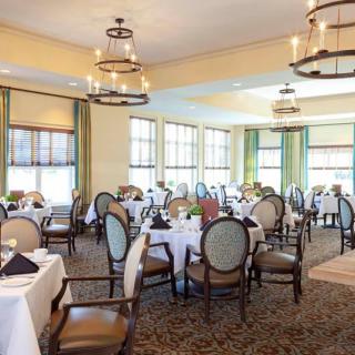 An elegant dining room with neatly arranged tables and chairs, illuminated by chandeliers.