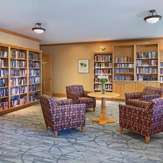 A cozy library room with bookshelves, comfortable chairs, and a table.