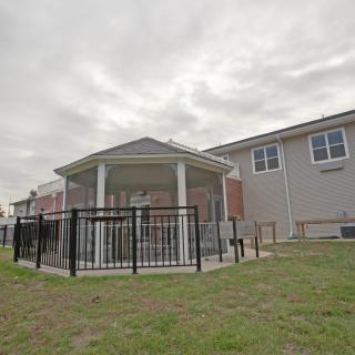 A backyard featuring a fenced gazebo adjacent to a house under a cloudy sky.