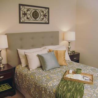 A cozy and well-decorated bedroom featuring a neatly made bed with multiple pillows, bedside lamps, and wall art.