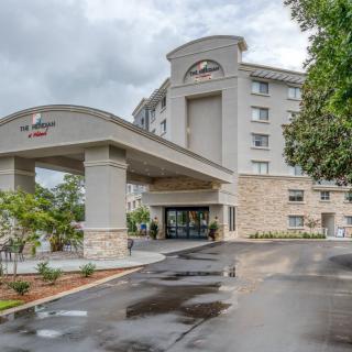 A modern hotel building with a grand entrance and surrounding greenery under a cloudy sky.