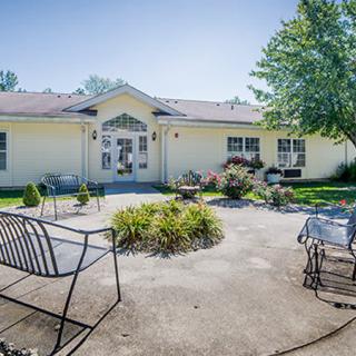 A sunny view of a building with a patio area featuring chairs and benches surrounded by a small garden.