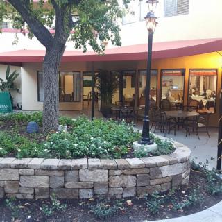 A charming courtyard with a stone wall and outdoor seating, surrounded by greenery and trees.