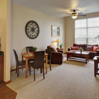 A cozy living room with a dining area, featuring comfortable seating, a coffee table, and a large window allowing natural light.