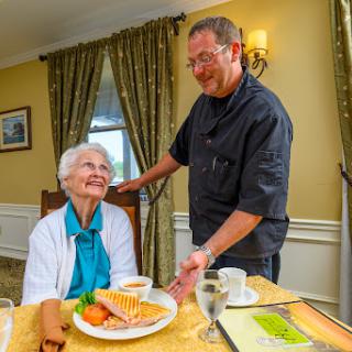 A caregiver serves a meal to an elderly woman, showcasing the warmth of dining experiences in assisted living.