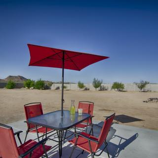 A patio set with red umbrella and chairs in a desert setting.