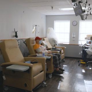 A patient sits in a comfortable chair in a medical treatment area, surrounded by other empty chairs.