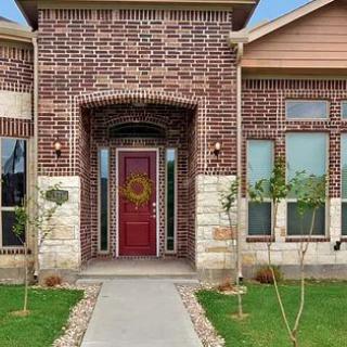 A brick house with a red front door and neatly landscaped yard.