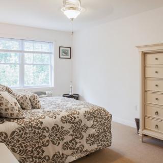 A well-lit bedroom featuring a bed with patterned bedding and a light wooden dresser.