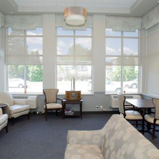 A spacious living room with large windows, furnished with a sofa, chairs, and a table.