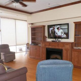 A cozy living room featuring comfortable seating, a television mounted above a fireplace, and wooden bookshelves.