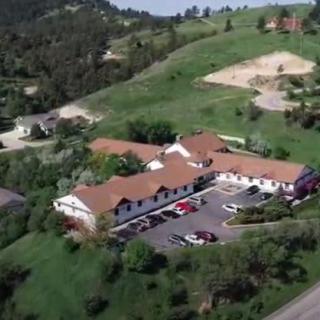 An aerial view of a building nestled in a hilly landscape with surrounding greenery and a parking lot.
