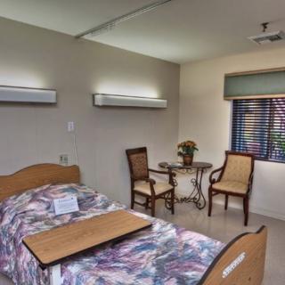 A hospital room with a patient bed, chairs, and a small table.