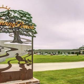 A scenic view of a golf course entrance with a decorative sign and a clubhouse in the background.