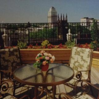 A cozy outdoor patio with a table and chairs overlooking a city skyline on a sunny day.