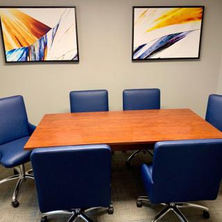 A modern conference room with a wooden table and blue office chairs, complemented by abstract artwork on the walls.